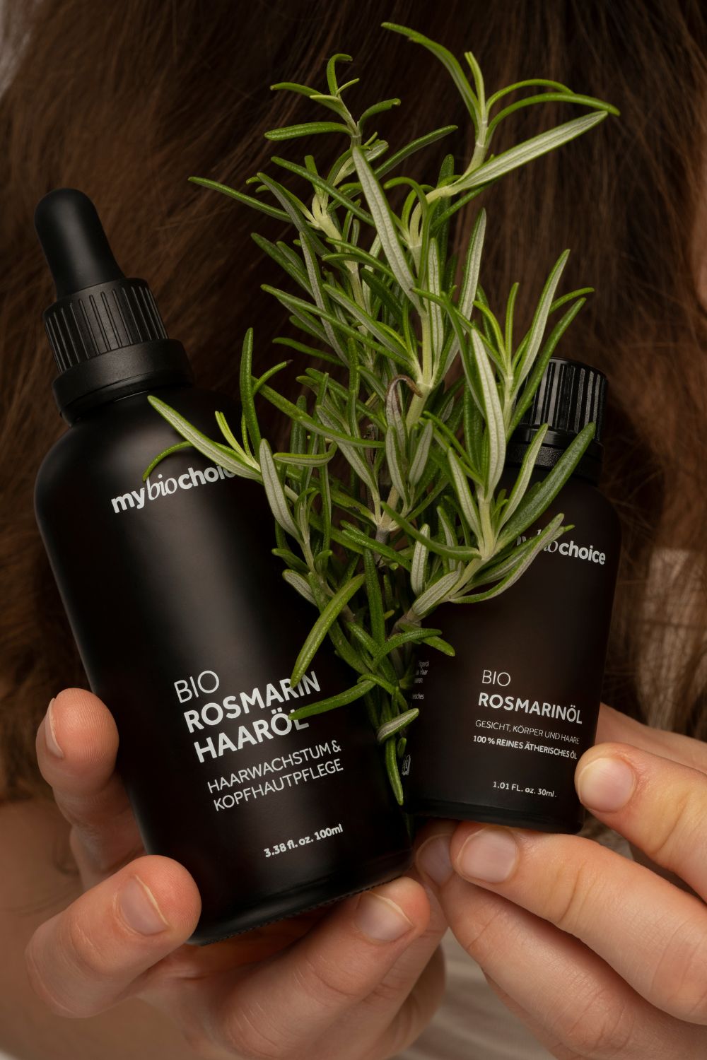 Zwei Glasflaschen mit Bio Rosmarin Haaröl und ätherischem Rosmarinöl von mybiochoice, dekoriert mit frischem Rosmarin.