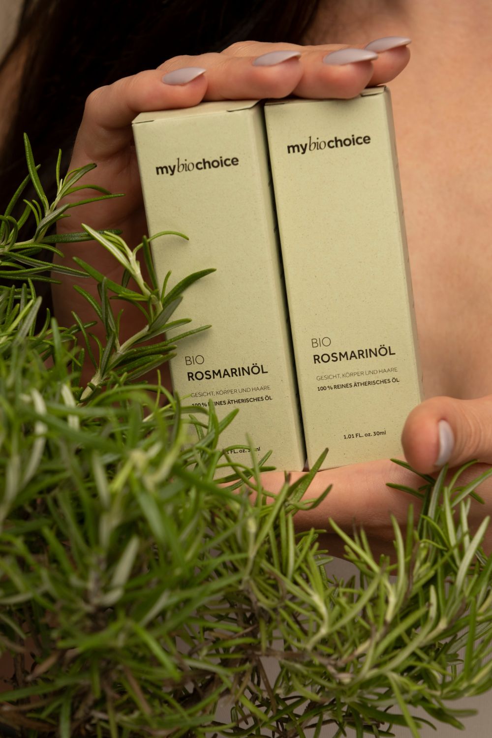 Zwei Verpackungen des Bio-Rosmarinöls von mybiochoice, gehalten von einer Frau mit Rosmarinzweigen im Vordergrund.