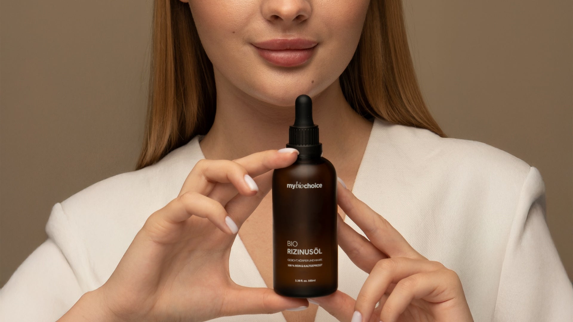 Eine Frau in weißer Kleidung hält eine Flasche Bio-Rizinusöl von mybiochoice mit beiden Händen vor ihrer Brust.