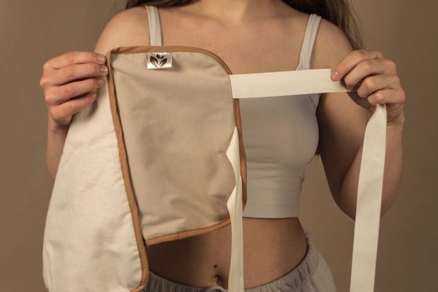 Frau zeigt die Innenseite eines naturfarbenen Leinen-Wickels mit Bindeband. Der Wickel ist weich gefüttert und wird zur Anwendung mit pflegenden Ölen wie Rizinusöl verwendet. Die offene Darstellung erklärt Aufbau und Handhabung.
