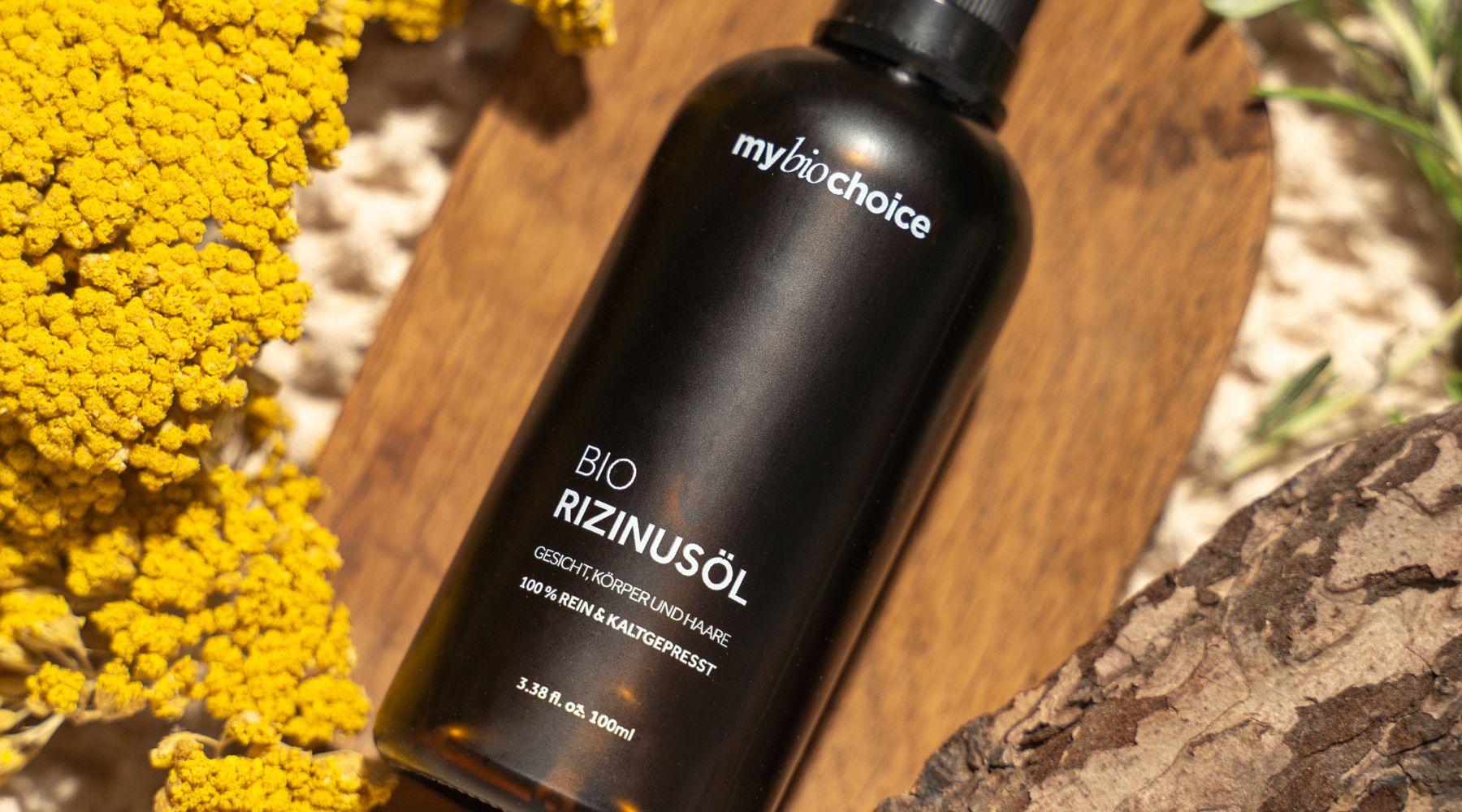 Bio Rizinusöl von mybiochoice auf hellem Stein mit gelber Blüte – hochwertiges, kaltgepresstes Naturöl für Haut und Haar.
