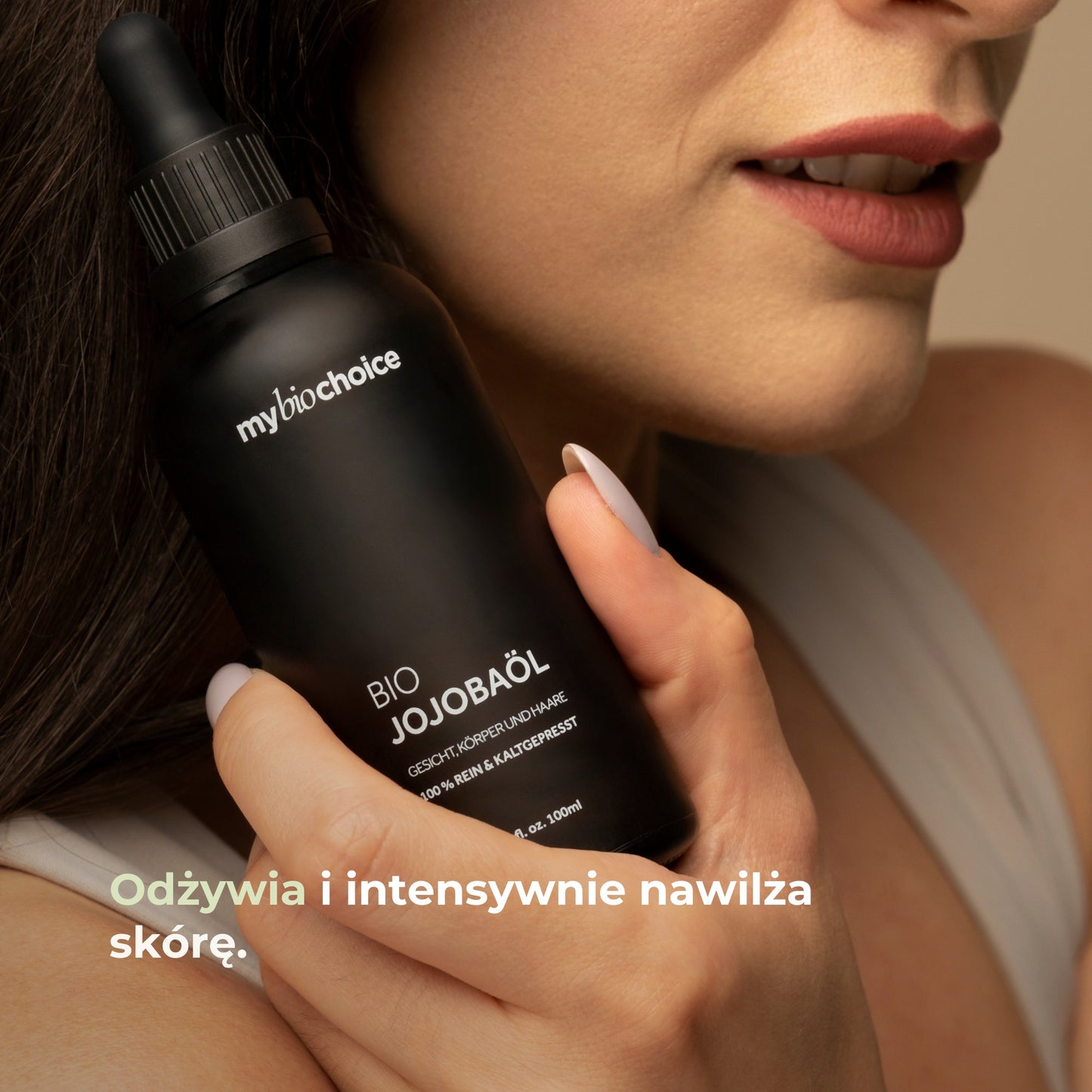 Kobieta trzymająca butelkę olejku jojoba od mybiochoice przy policzku