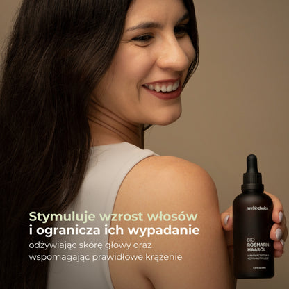 Uśmiechnięta kobieta z gęstymi włosami prezentuje olejek rozmarynowy mybiochoice wspomagający wzrost włosów.